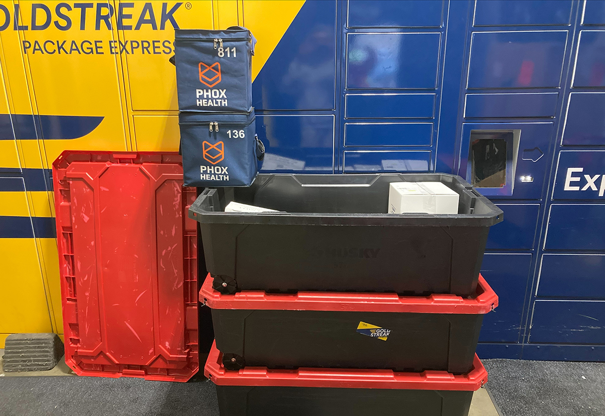 Blue PhoxBox totes on shipping bins in front of a blue and yellow wall with a GoldStreak Package Express logo.